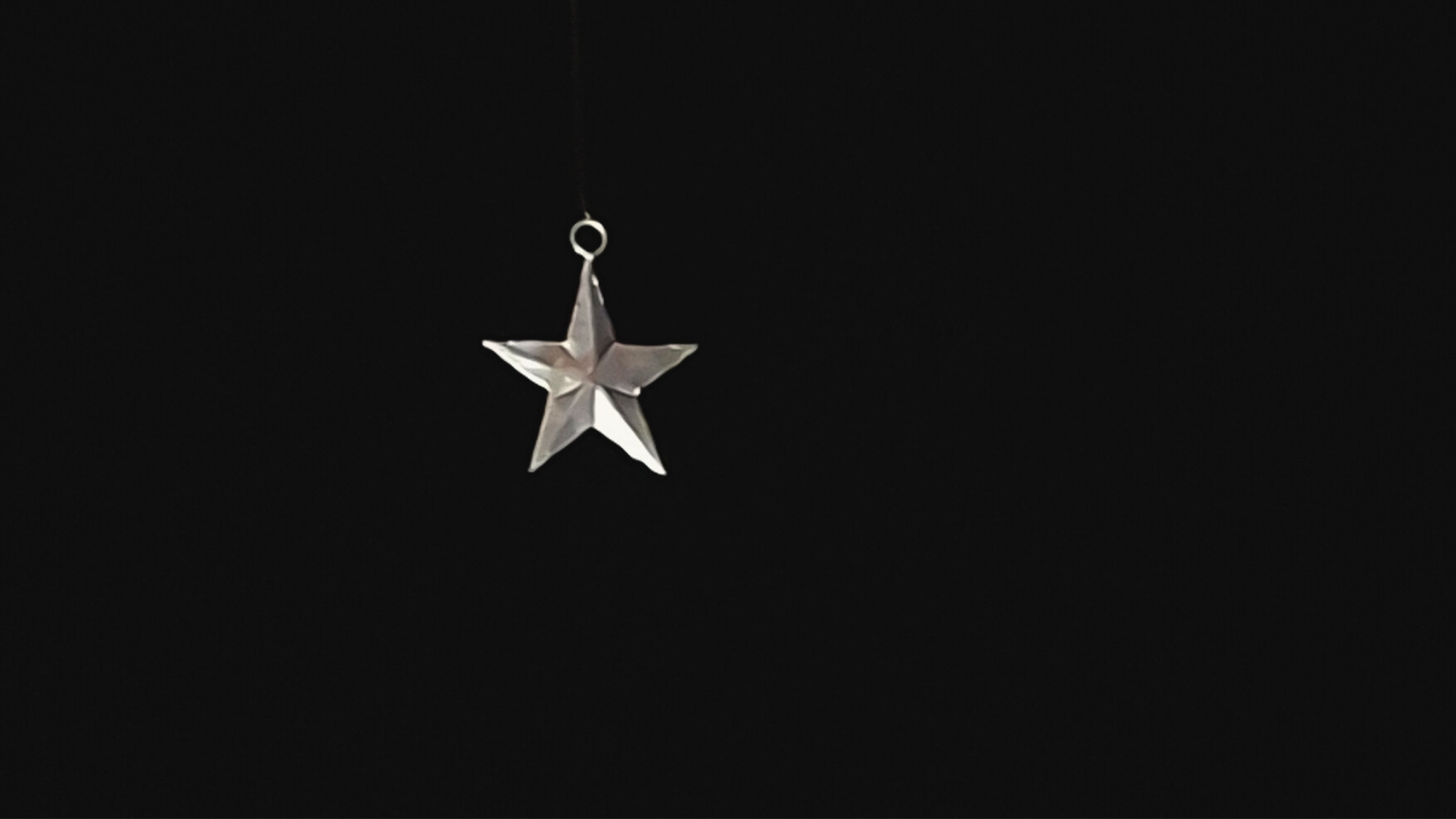 A single metal star hanging in the dark, softly lit, suggesting quiet presence and threshold.
