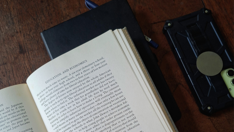 Open book on a wooden table with a phone placed face-down beside it