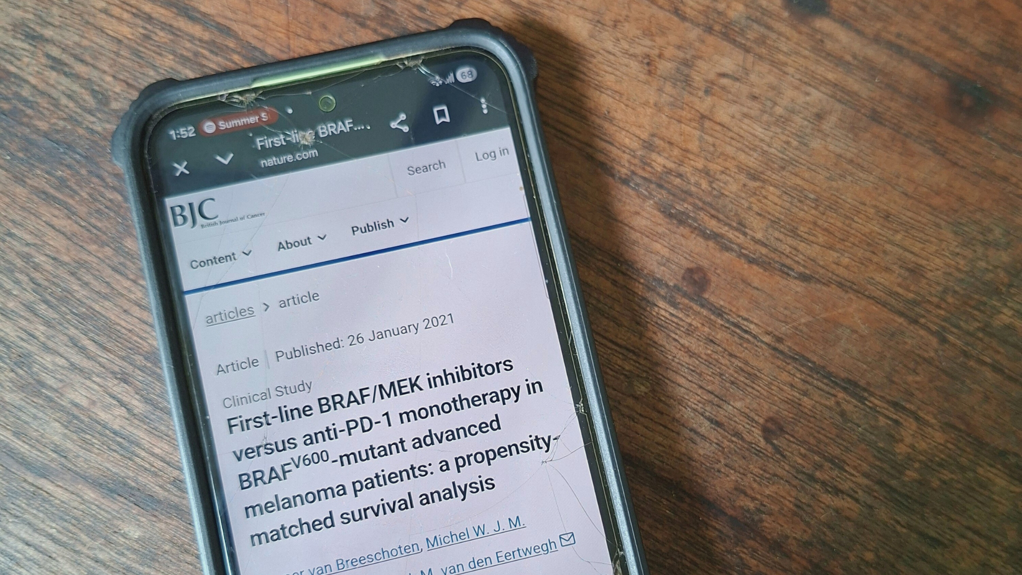 Mobile phone displaying British Journal of Cancer article on BRAF/MEK inhibitors and anti-PD-1 therapy on a wooden table surface.