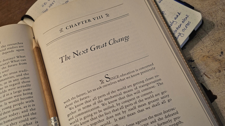 Open book showing chapter "The Next Great Change" with pencil on wooden table, Conversations reading essay by Jo-Anne.