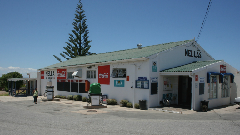 A white roadside shop building viewed from an angle, entrance and quiet street in natural daylight.