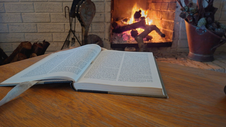 Open book beside a fire in a quiet room, used for a reflection on decision pressure and how conflict restarts.