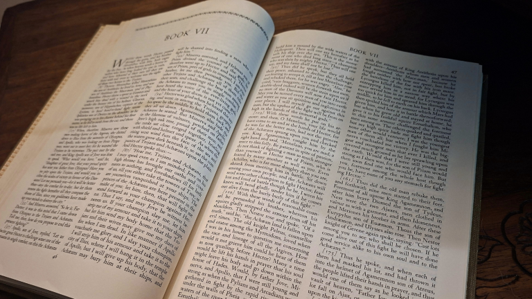 Open copy of The Iliad on a wooden table, turned to Book VII.