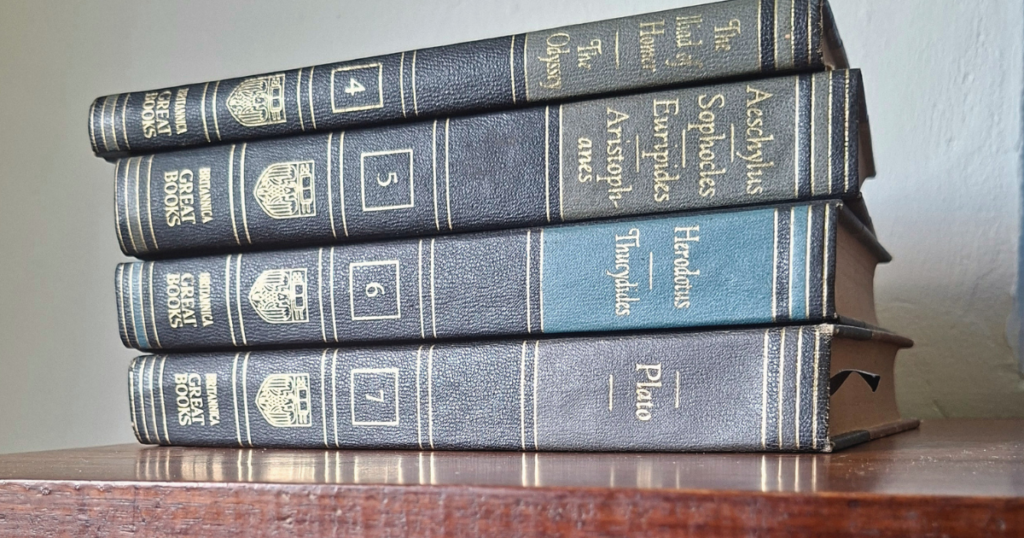 A stack of Great Books on a wooden shelf, including works by Aeschylus, Sophocles, Euripides, Herodotus, Thucydides, and Plato